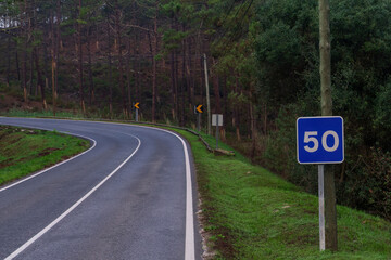 Road with a blue road sign with the number 50 among the hills covered with coniferous forests