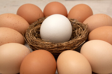 Food photo for Happy Easter holiday. White chicken Easter egg lies in the nest. Beige and brown eggs lie around the nest on an old vintage white wooden table with cracks and scuffs. Village farm. Diet
