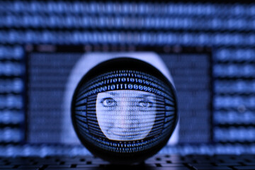 Concept for AI artificial intelligence or operating system or identity theft online. A female face in the midst of binary data stream on a computer screen as seen through a lens ball.