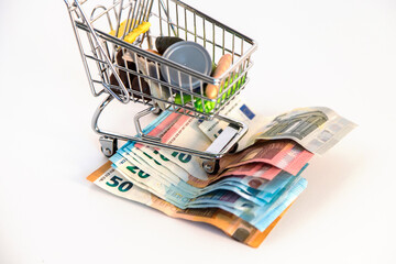 Supermarket shopping cart with essential goods and several euro banknotes on a white background. Conceptual image about purchasing power, family expenses, essential goods,consumer society. Copy space
