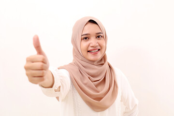 Happy young asian muslim woman standing while showing thumbs up. Selective focus. Isolated on white