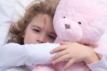 Child wakes up with toy teddy bear from sleep in bed. Kid wakes up in the morning in the bedroom. Favorite toy for sleep.