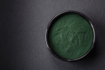 Spice, green color spirulina in the form of powder in a black bowl