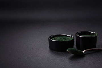 Spice, green color spirulina in the form of powder in a black bowl