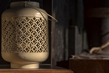 Stary lampion ze stalowej blachy , o ażurowej konstrukcji, stojący na nieco zakurzonej , drewnianej , lakierowanej półce .  