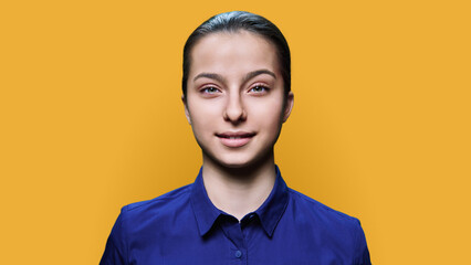 Headshot portrait of smiling teenage girl 15, 16 years old on yellow background