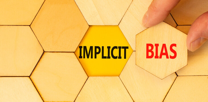 Implicit bias symbol. Concept words Implicit bias on wooden puzzles. Beautiful yellow table yellow background. Businessman hand. Business psychology implicit bias concept. Copy space.