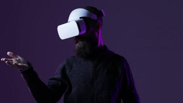 Young man in futuristic costume on dark background. Guy using VR helmet. Augmented reality, virtual reality, future technology, game concept. 