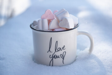 A cup of hot chocolate and marshmallows stands in the snow. Winter concept.