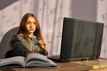 The girl is sitting at the table and looking at the laptop.
