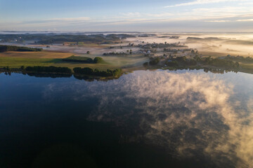Foggy morning on a beautiful lake surrounded by forests and fields. A small village located near a lake in fog and morning sun.