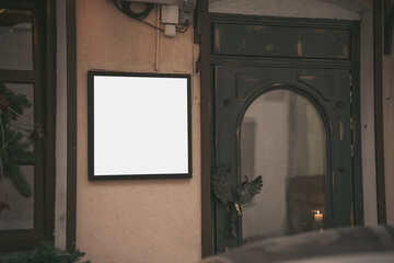 White blank display in wooden frame mounted on wall next cafe entry outdoor. Street restaurant menu near building door outside.