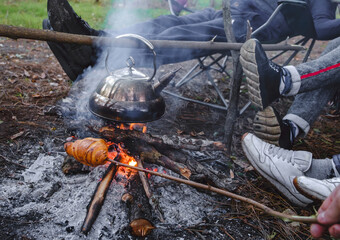 Young and cheerful friends sitting at bonfire , boil the kettle and fry bread on the nature....