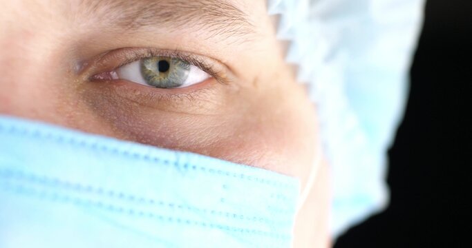 Half Face Of A Doctor In A Mask On A Black Isolated Background. The Doctor Looks Into The Camera On A Black Background. Handsome Doctor Man With A Serious Look.