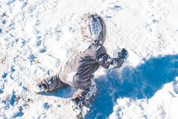 Dziecko ubrane w kombinezon zimowy, bawiące się w śniegu.