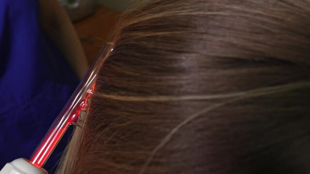 Comb darsonval. Skin medical procedure. A woman in a red shirt is combing her hair in front of a mirror with an electric device.