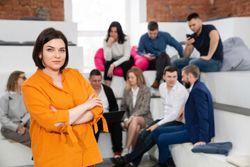 a brunette woman in an orange blouse with men and women in the office.