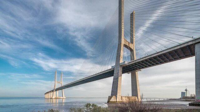 Vasco da Gama bridge timelapse hyperlapse with reflection on water and blue cloudy sky. Cable-stayed bridge and Tagus river. Lisbon, Portugal.