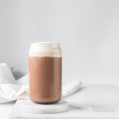 Mocha latte with whipped cream in a can shaped glass, iced mocha with foam on a table