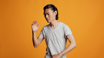 Positive person showing robotic dance moves on camera, acting silly like robot over orange background. Happy carefree guy dancing with funny energy in studio, active funky dancer.
