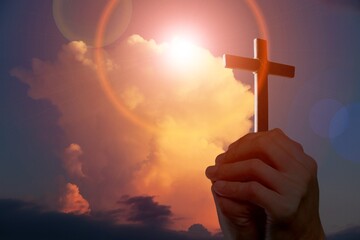 A hand holds a wooden cross on sky background