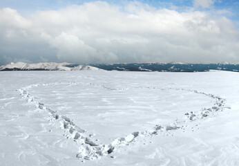 Human footprint form the heart shape on snow-covered mountainside plateau and mountain ranges...