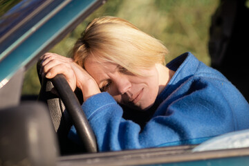 Tired woman driving a car. A middle-aged woman in her forties leaned over the steering wheel of a...