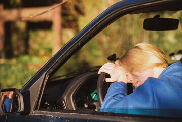 Tired woman driving a car. A middle-aged woman in her forties leaned over the steering wheel of a car. Fatigue, exhaustion, rest during the trip.