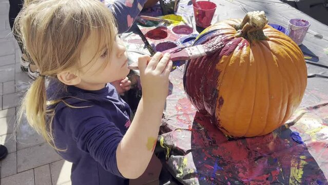 Preschool girl in blue t-shirt paints a pumpkin