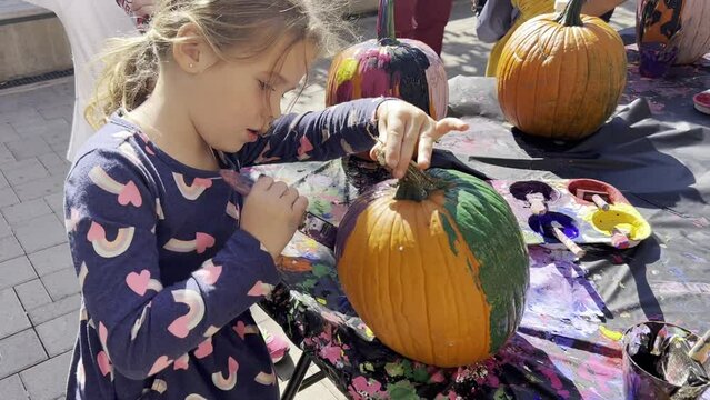 Elementary school girl in heart pattern dress paints a pumpkin