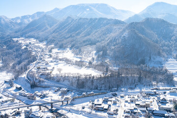 High Angle Landscape of Railway bridge the over the river passing small town in snow day. Pine tree forest mountain with railroad track covered in snow. Beautiful scenic nature in winter season.