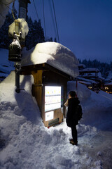 Fototapeta premium Asian girl in winter coat choosing and buying hot drinks in beverage vending machine covered in snow during travel small town at night. Young woman travel local village in Japan on winter vacation.