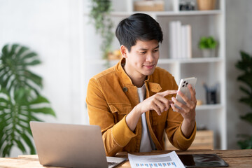 Portrait of young handsome Asian man using his asmartphone while working in comfortable office room.