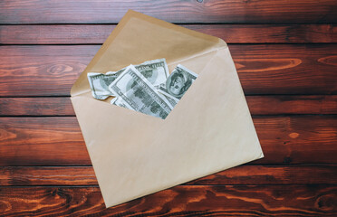 Old large craft beige envelope with dollar bills lies on a brown table. The concept of a bribe, donation, alimony. View from above.