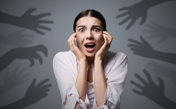 Paranoid delusion. Scared woman screaming on grey background. Shadows of hands reaching for her symbolizing fear and anxiety