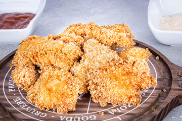 Delicious fried chicken on a rustic wooden board with tomato sauce and mayonnaise on a marbled background