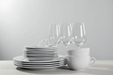 Set of clean dishware and glasses on white wooden table against light background