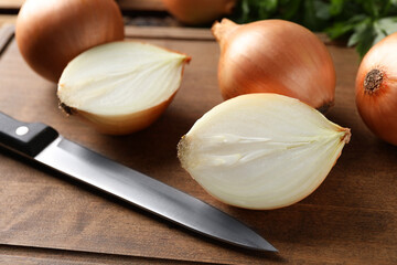 Whole and cut onions with knife on wooden board, closeup