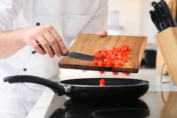 Chef putting cut tomatoes into frying pan indoors, closeup