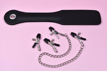 Silver nipple clips and spanking device on a pink background, slave spank paddle, accessories for adult sexual games, sex toys for BDSM, adult whip