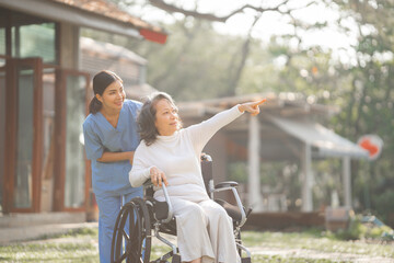 Young asian care helper with asia elderly woman on wheelchair relax together park outdoors to help and encourage and rest your mind with green nature.