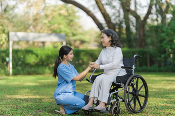 Young asian care helper with asia elderly woman on wheelchair relax together park outdoors to help and encourage and rest your mind with green nature. hold hands to encourage
