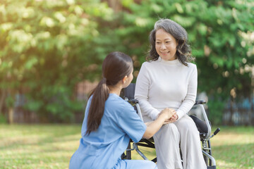 Obraz premium Young asian care helper with asia elderly woman on wheelchair relax together park outdoors to help and encourage and rest your mind with green nature.