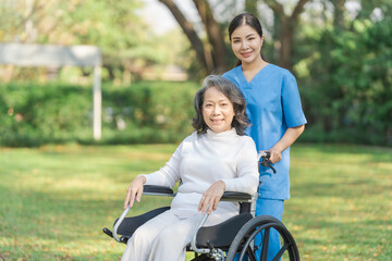 Young asian care helper with asia elderly woman on wheelchair relax together park outdoors to help and encourage and rest your mind with green nature. Looking camera.