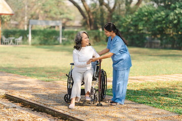 Young asian care helper with asia elderly woman on wheelchair relax together park outdoors to help and encourage and rest your mind with green nature.