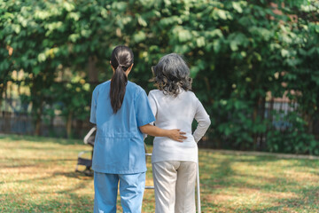 Young asian care helper with asia elderly woman on wheelchair relax together park outdoors to help and encourage and rest your mind with green nature. Help support yourself to learn to walk. walker