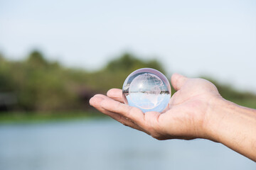 Naklejka premium Crystal globe in male hand and on river background.