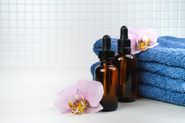 Shower gel,  towel and soft bath, body sponge and shampoo in the bath on a white tile. Composition with body care accessories and beauty products. Oil for face and body. Orchid flowers