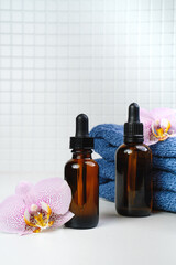 Shower gel,  towel and soft bath, body sponge and shampoo in the bath on a white tile. Composition with body care accessories and beauty products. Oil for face and body. Orchid flowers