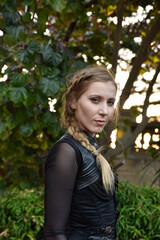 Close up portrait of beautiful female model with blonde plait, wearing black leather catsuit,...